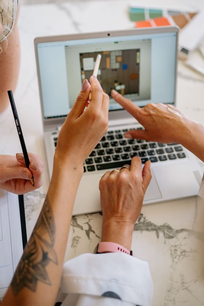 Hands pointing and touching a laptop screen during a planning session on a marble table.